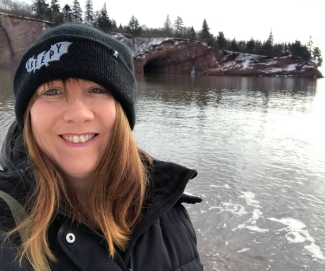 Woman in black winter jacket and tuque at the side of a river