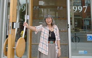 A woman smiles as she holds open the glass door to a building.