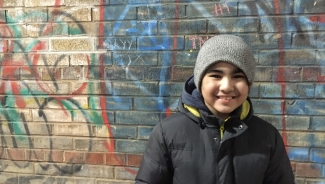 Aary standing outside smiling against a graffiti wall