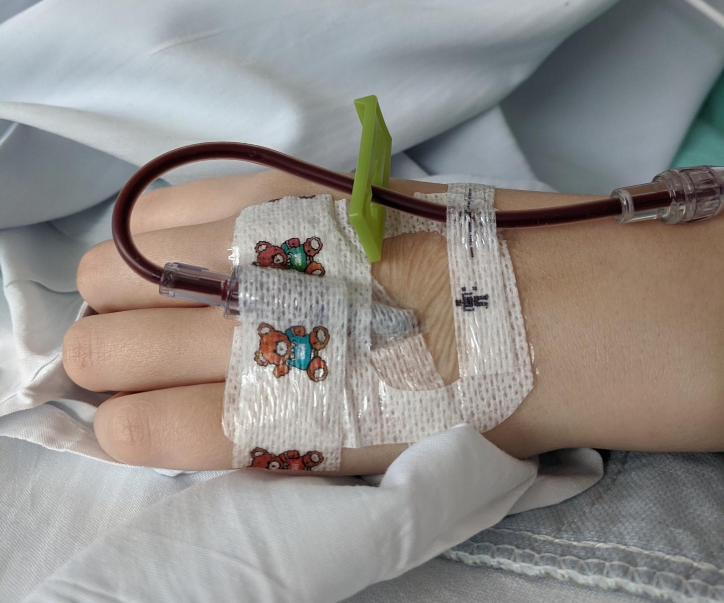 Child's hand with colourful bandage and tubes during blood transfusion