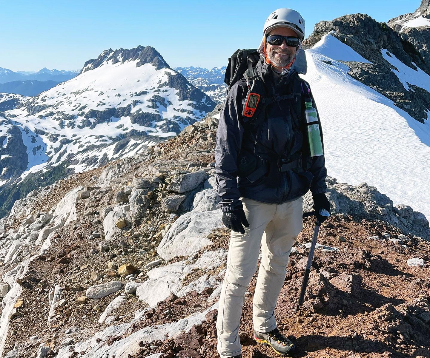 Man in sunglasses and helmet on mountain with peaks behind