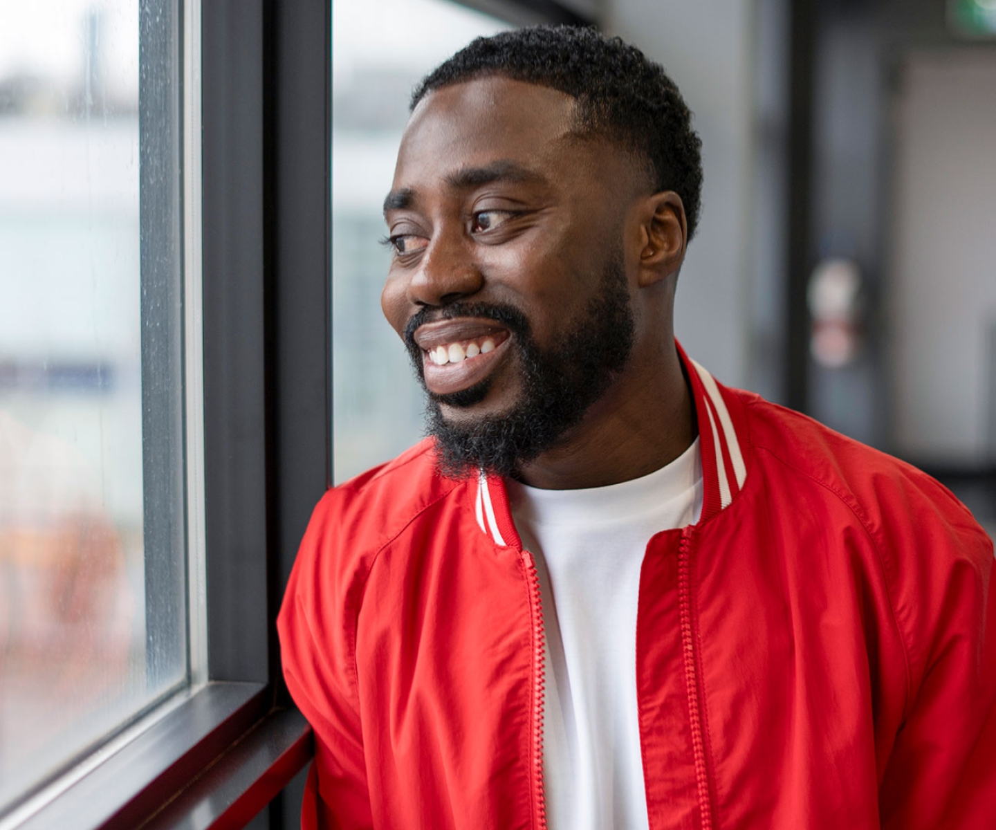 Man in red jacket smiling and looking through window