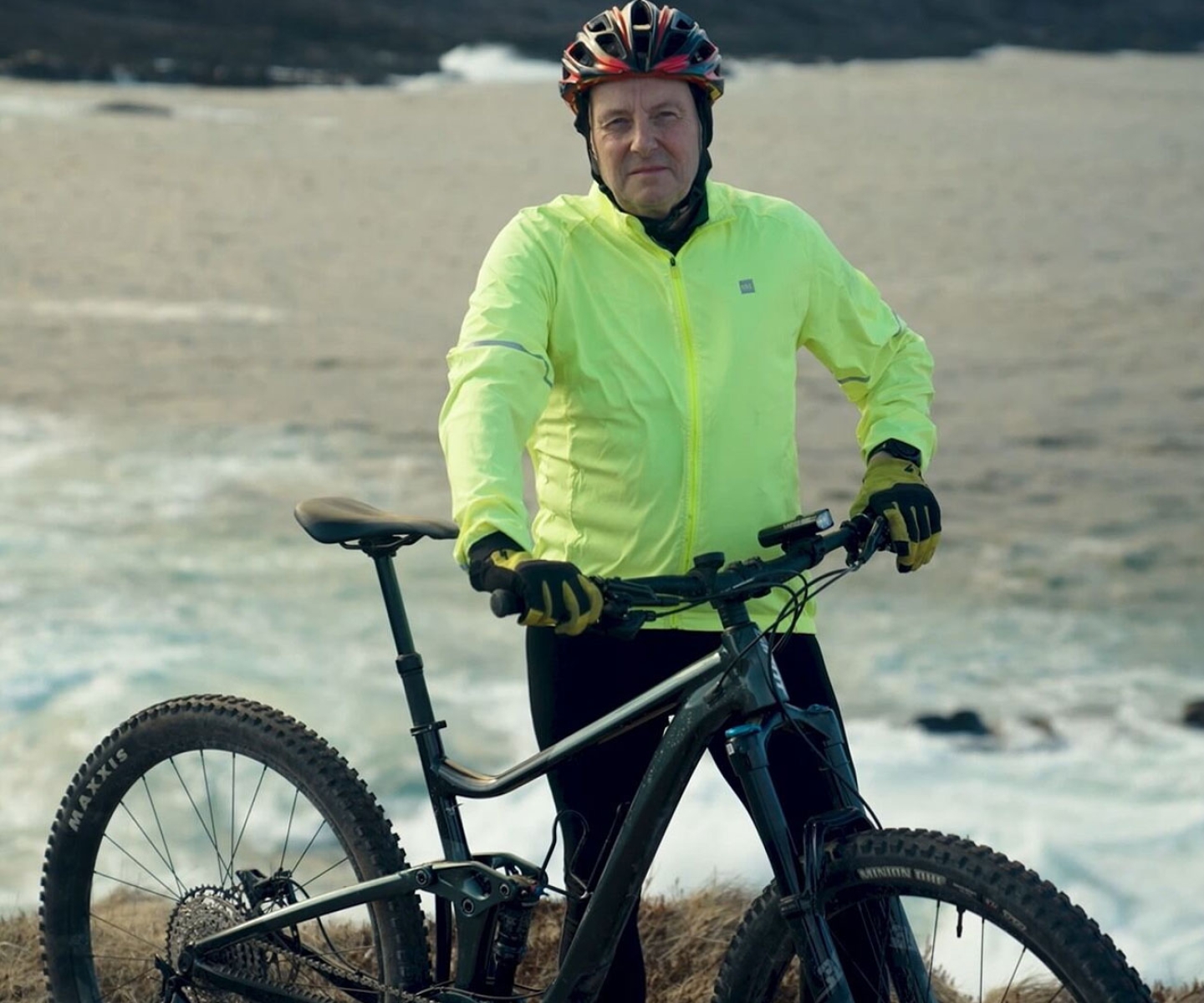 Man in yellow jacket stands with bicycle near ocean