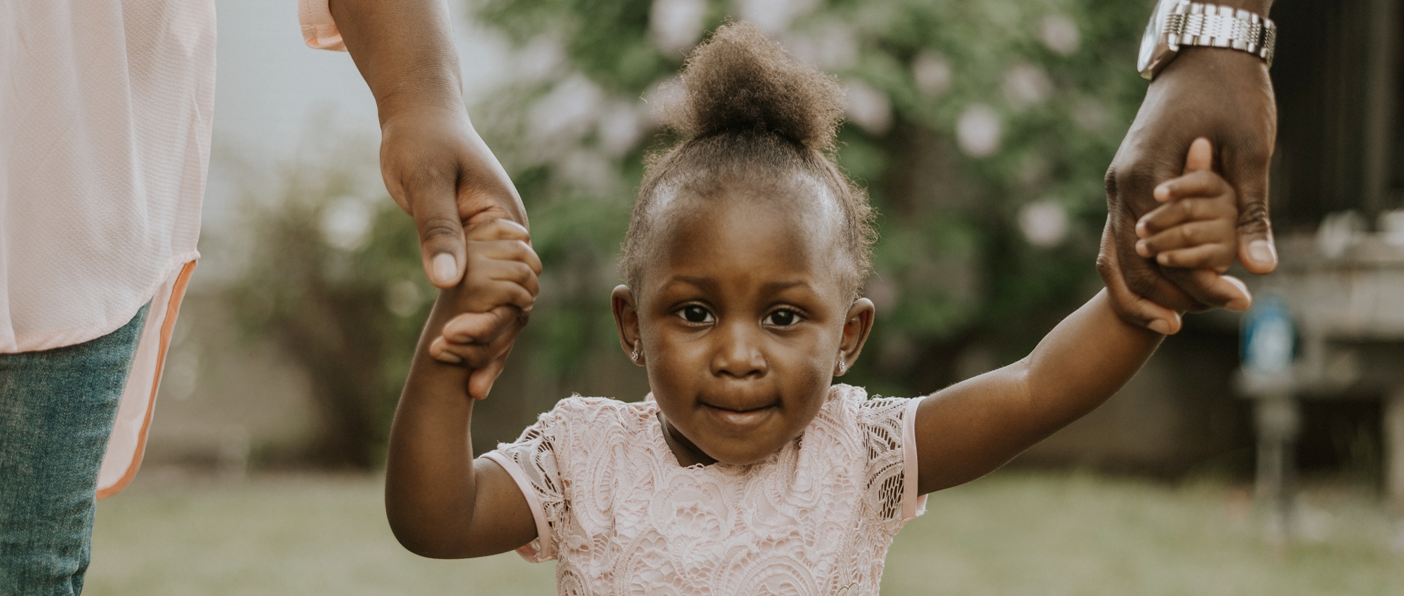 Two adults who donate blood hold the hands of a child who received blood transfusions outdoors