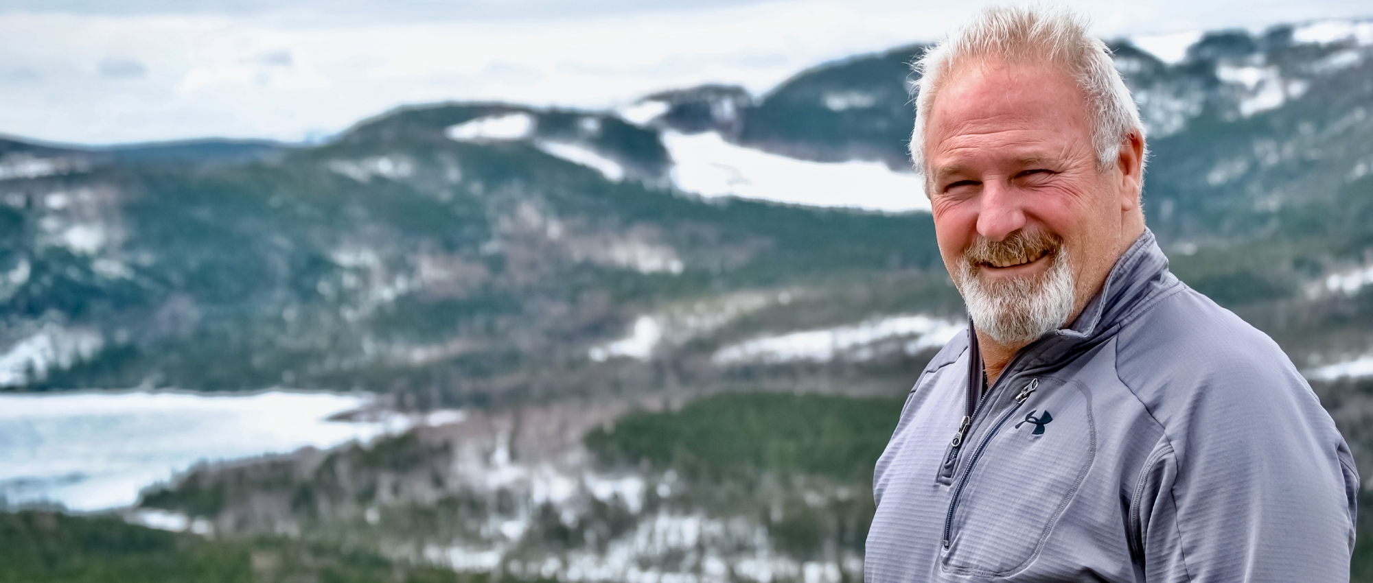 Featured image of plasma recipient Kirby Graeme standing outside where behind him is a beautiful scenic mountain