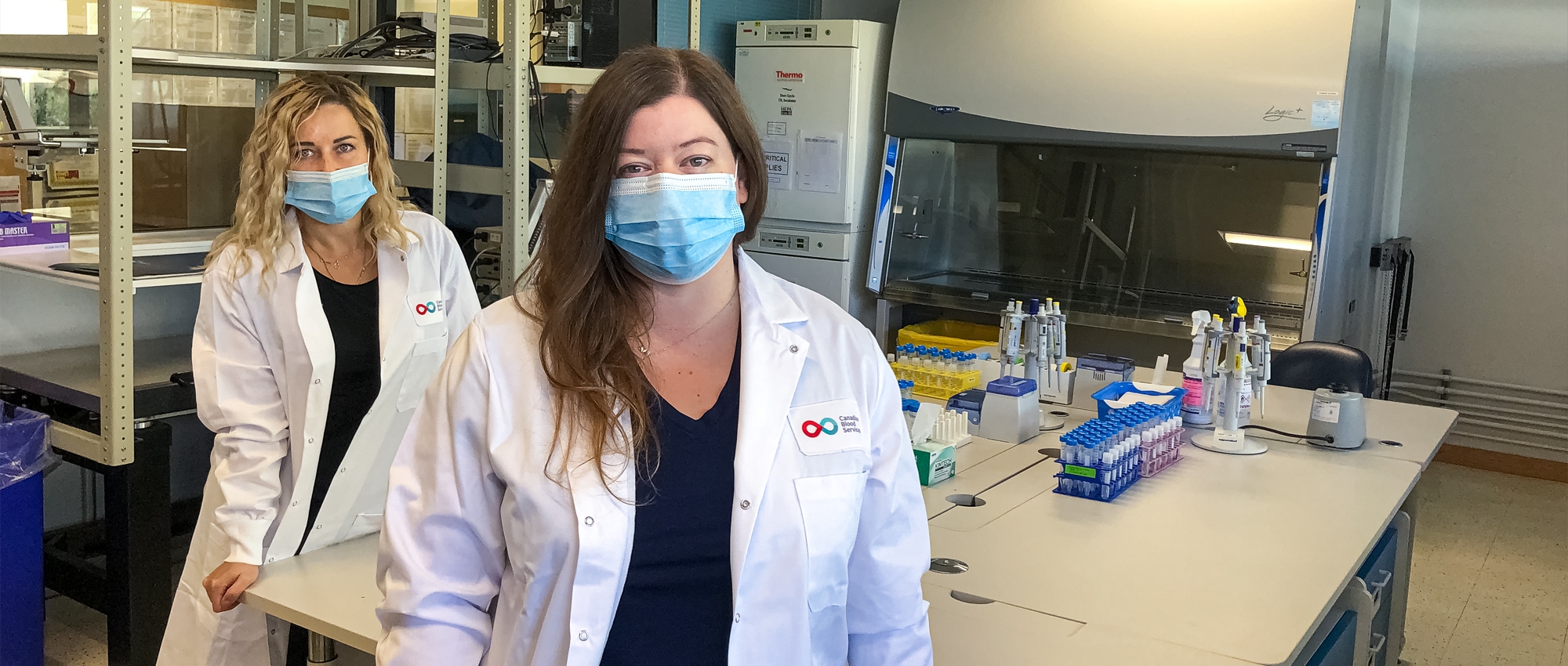 Image of Lab researchers Dr. Olga Mykhailova and Tracey Turner standing in the lab with a bunch of empty test tubes on the table.