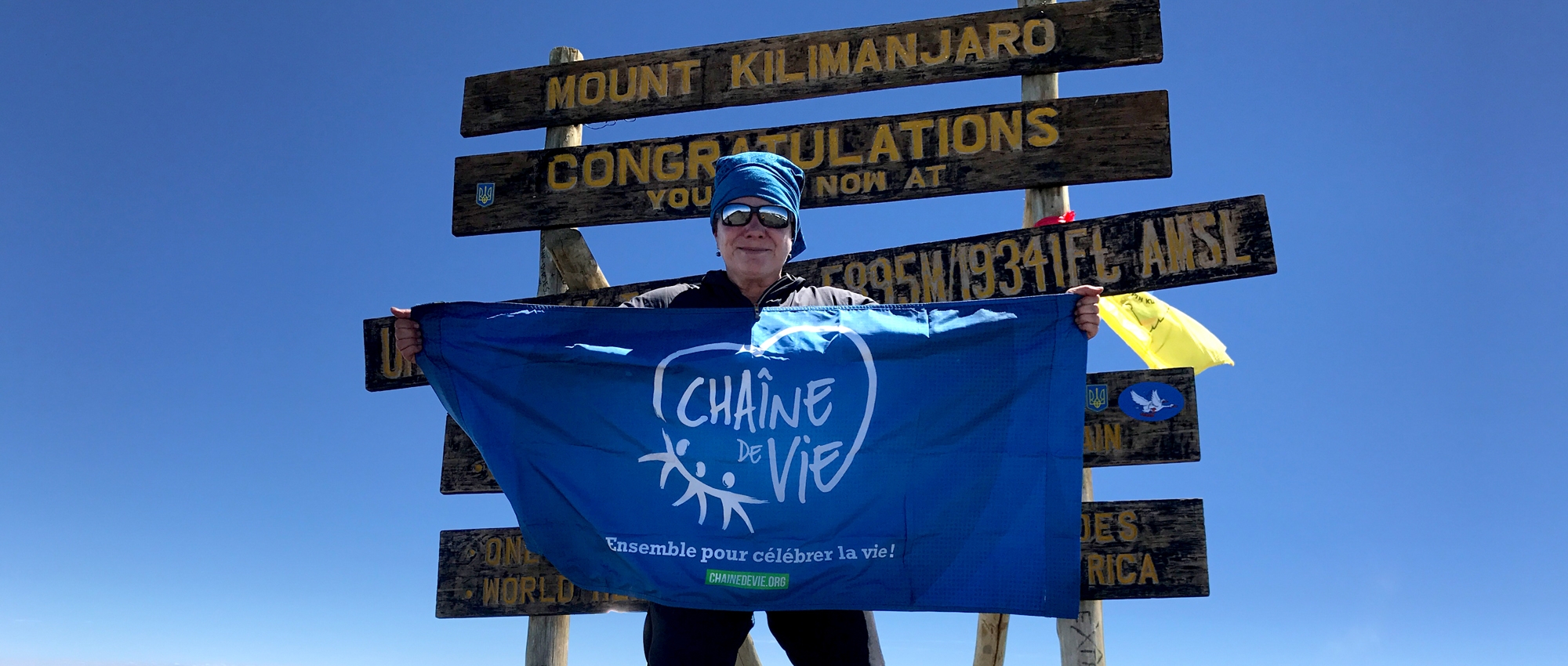 Lucie Dumont stands on top of Mount Kilimanjaro holding the Chain of Life flag.