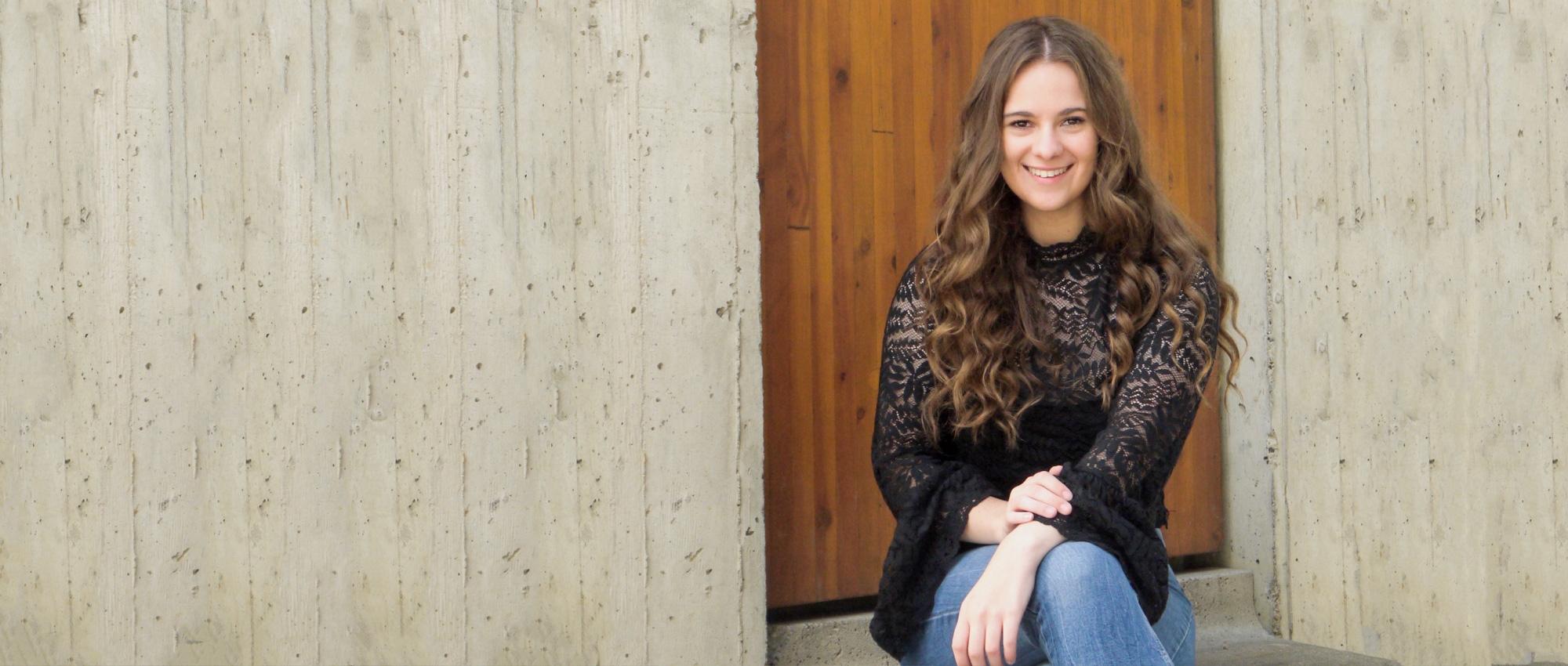 A young woman who survived childhood cancer sits on a step in front of a door. 