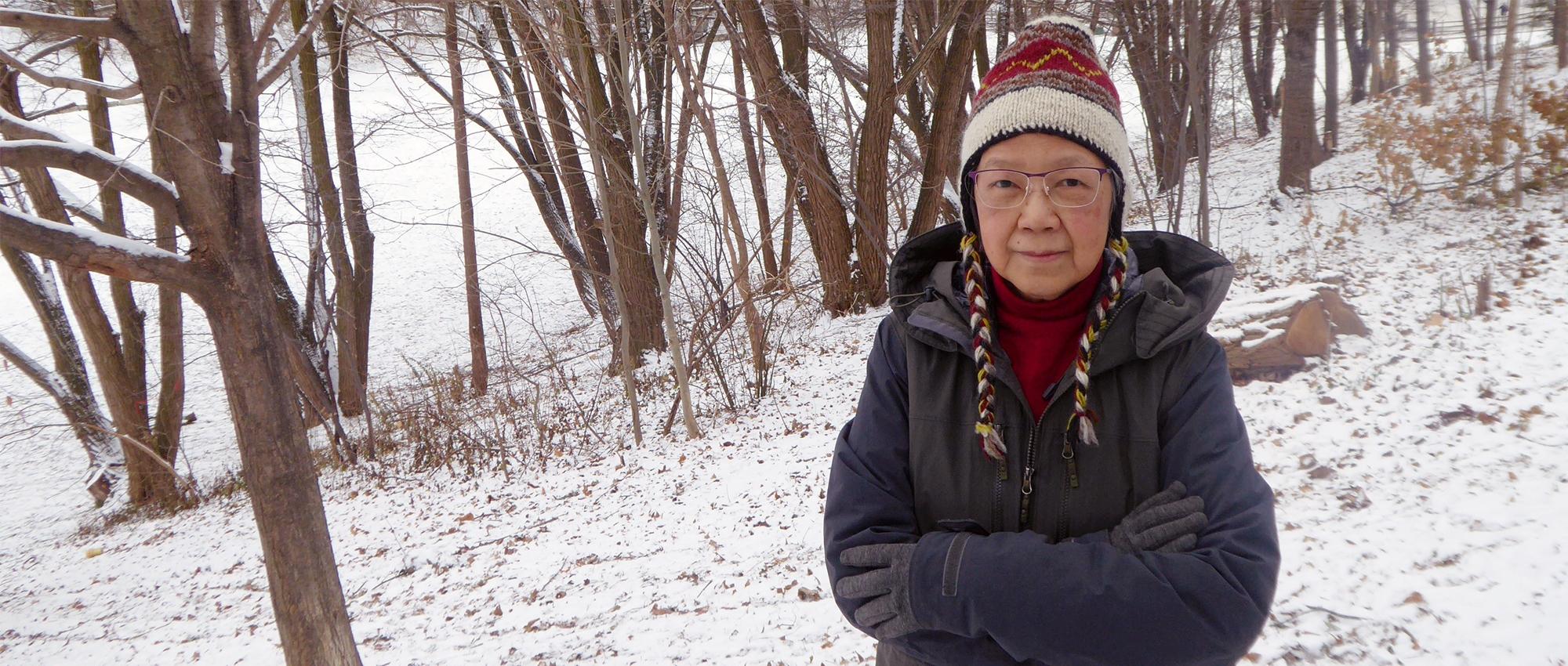 A woman in winter coat and hat standing in a snowy wooded area