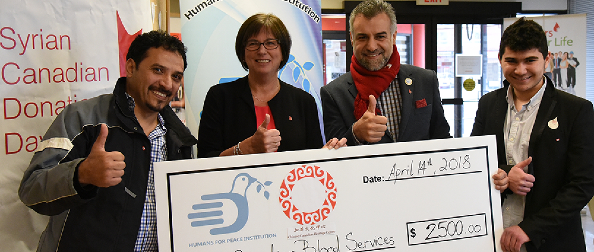 4 people standing and holding a cheque made out to Canadian Blood Services for 2500 as part of Syrian Canadian Donation Day