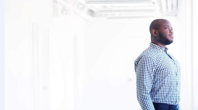 Charles with a blue checker dress shirt standing inside in an open space looking outward