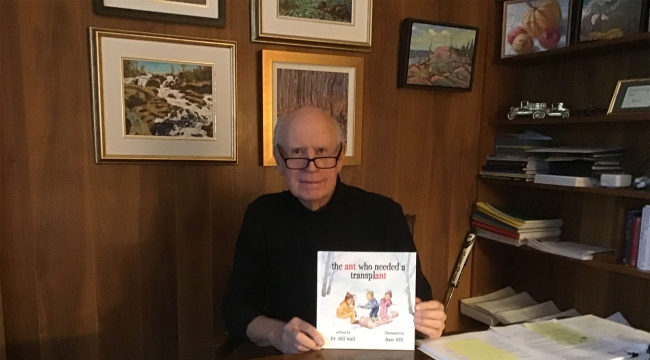 Dr Wall à son bureau tenant un exemplaire de son livre pour enfants intitulé the ant who needed a transplant.