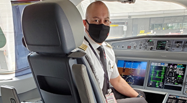 Air Canada pilot sits in his chair in the flight deck of a plane. A blue cooler containing a donated kidney is placed behind his chair.  