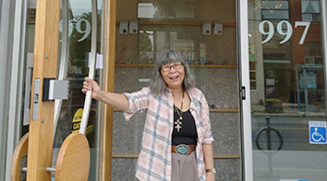 A woman smiles as she holds open the glass door to a building.