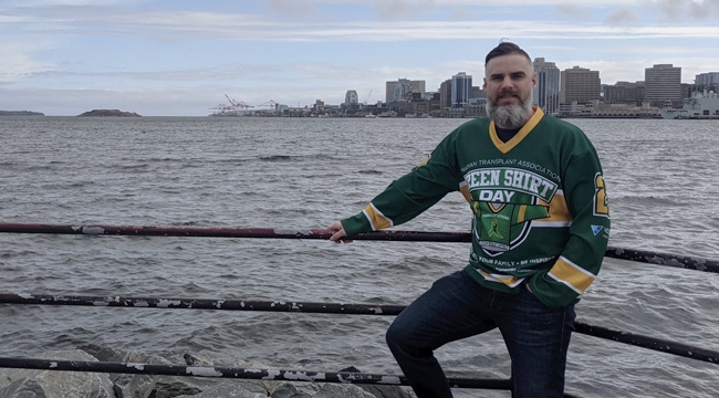 A man wearing a green shirt day jersey, in front of a body of water with a city skyline in the background.