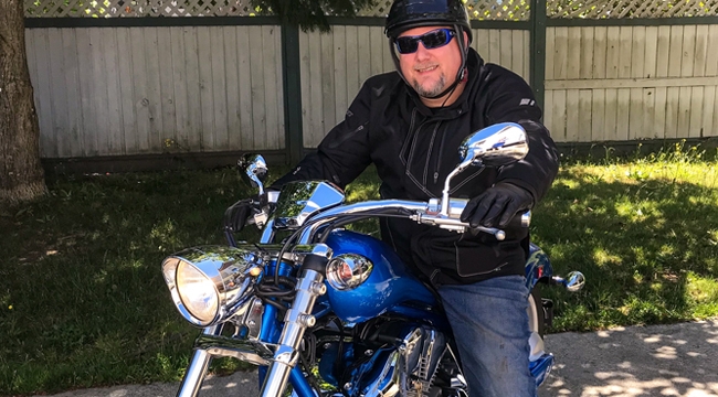 Thumbnail image of blood recipient Nathan Olson posing on his motorcycle wearing full motorcycle gear.