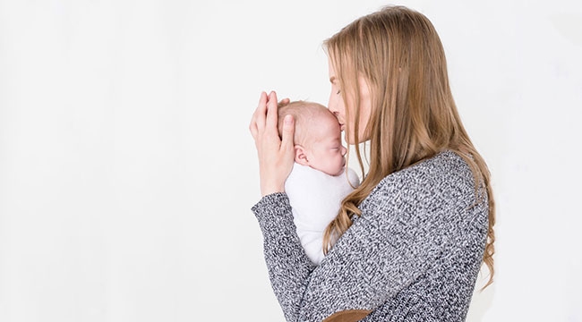 Mother holding swaddled baby and kissing his head