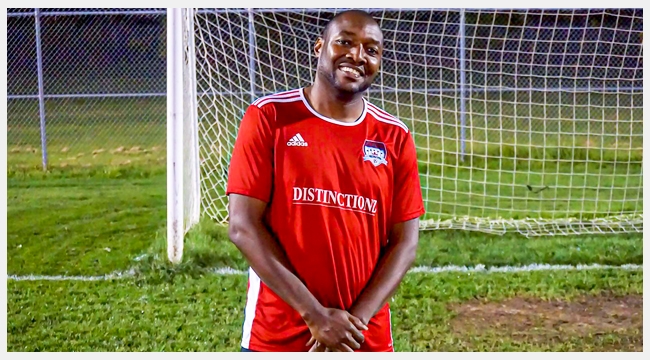 Image of Dujon Donaldson wearing a red soccer uniform in front of a soccer goal post