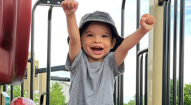 Boy smiling with outstretched arms on playground slide. 