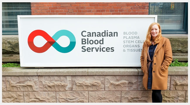 Dr Kelly Holloway standing beside a Canadian Blood Services Sign outside